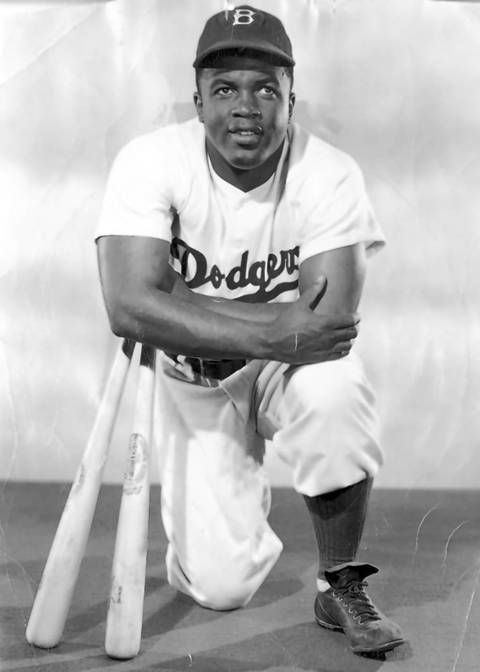 a black and white photo of a baseball player with his bat leaning on the ground