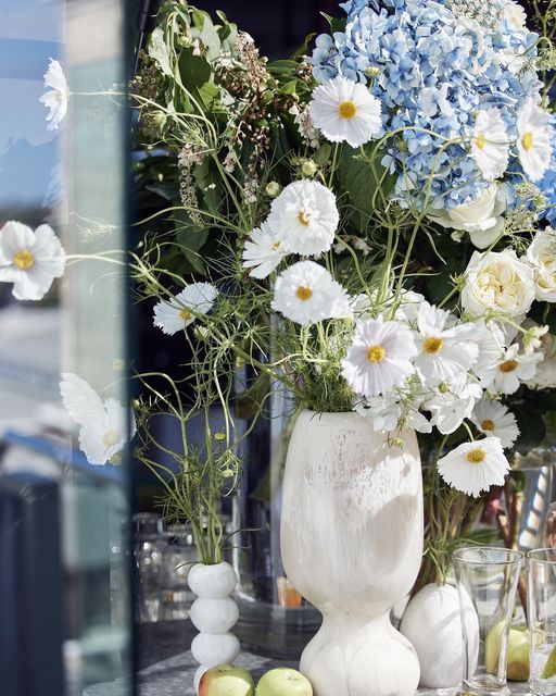 a vase filled with white and blue flowers on top of a table next to apples