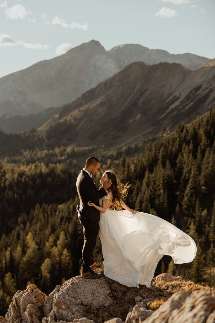 a bride and groom standing on top of a mountain