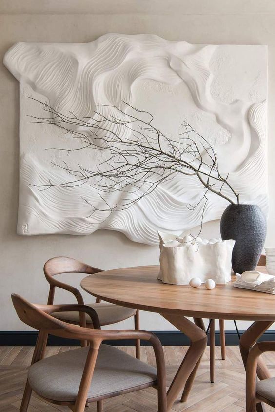 a dining room table with two vases on it and a wall sculpture behind it