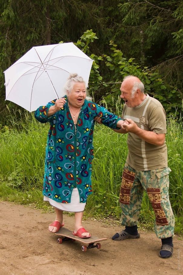 an older woman holding an umbrella and standing next to a man on a skateboard