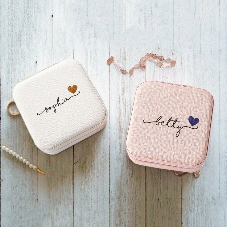 two pink and white jewelry cases sitting on top of a wooden table next to pearls