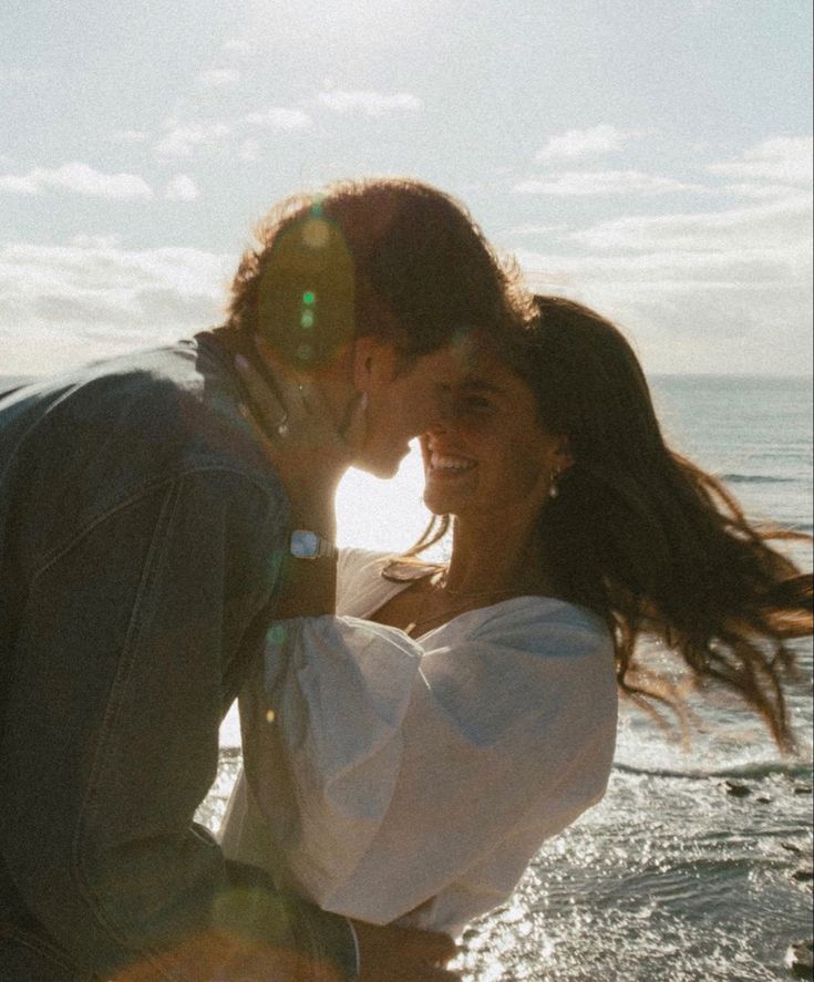 a man and woman kissing on the beach with sun shining in the sky behind them