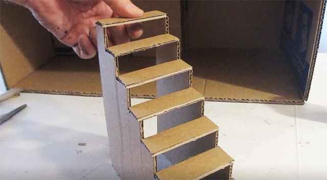 a hand is reaching up to open a cardboard box with stairs in the bottom half