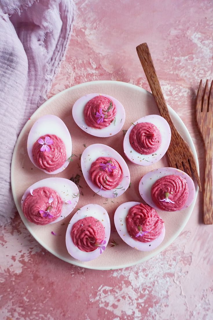 deviled eggs with pink frosting on a plate next to cinnamon sticks and an egg whisk