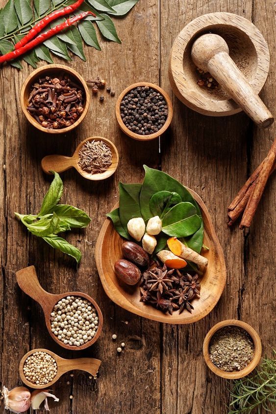 various spices and herbs in wooden spoons on a table