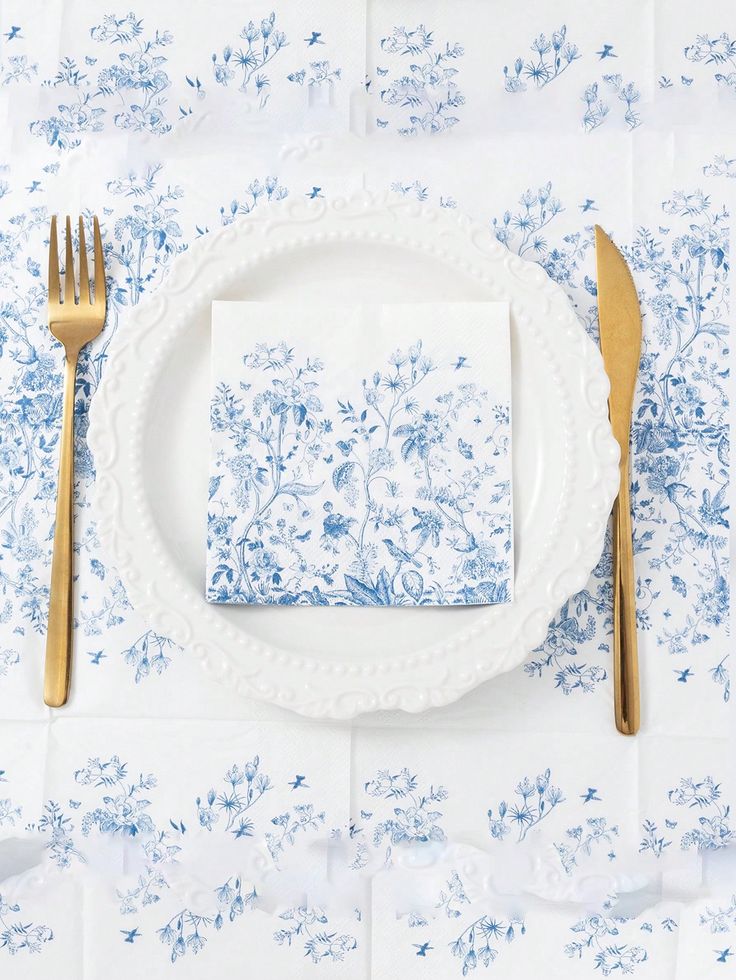 a place setting with blue and white floral napkins, silverware and gold forks