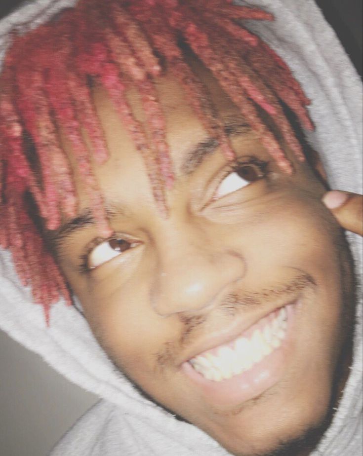 a man with red dreadlocks and a white hoodie smiles at the camera