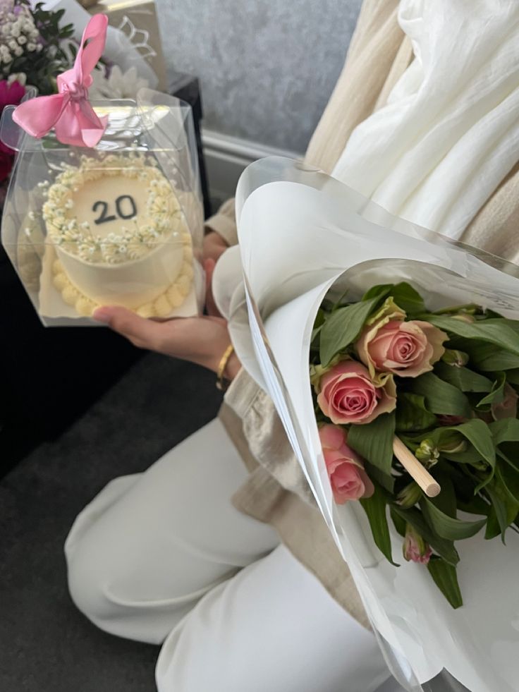 a woman holding a bouquet of roses and a cake in her hand with the number 20 on it