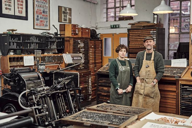 two people standing next to each other in a room full of old typewriters