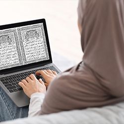 a person sitting on a bed using a laptop with an open book in front of them