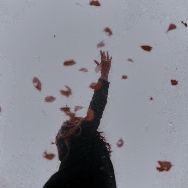 a woman reaching up into the sky with her hands in the air and falling leaves