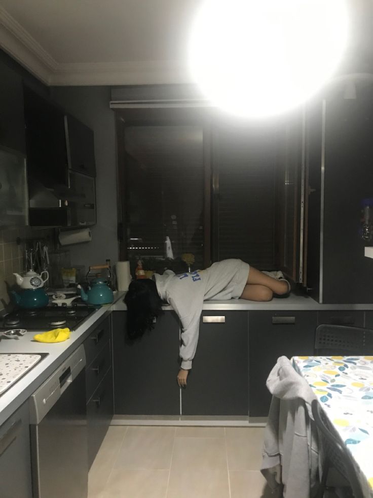 a person laying on the kitchen counter in front of a light that is turned on