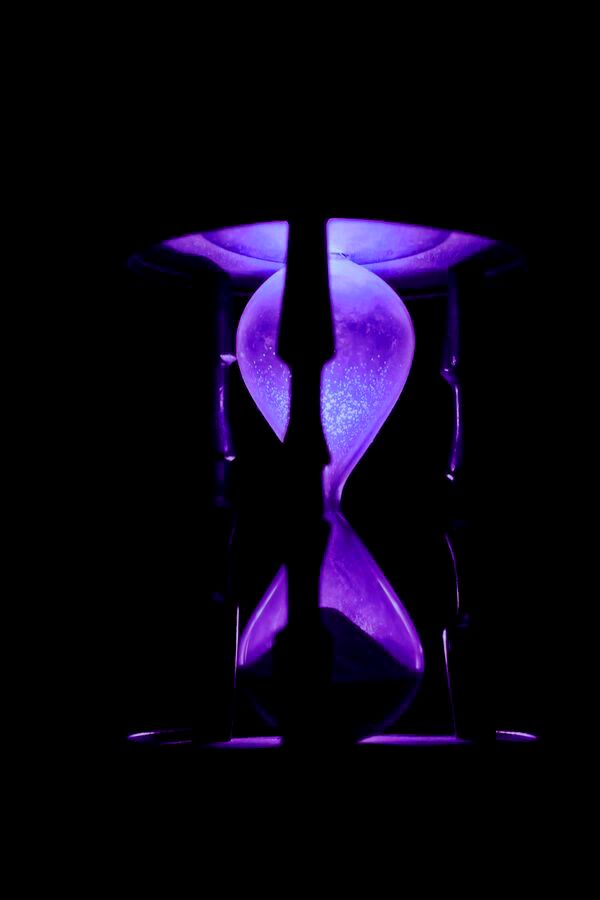 an hourglass sitting on top of a table with purple light in the dark behind it