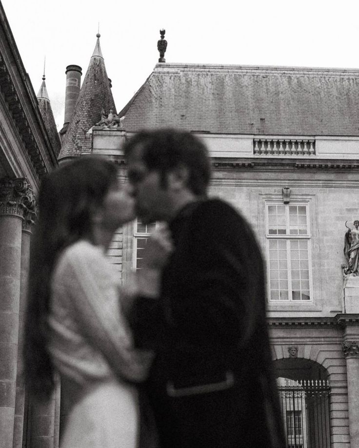 a man and woman standing next to each other in front of a building