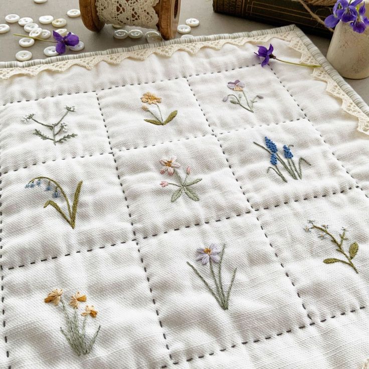 a quilted table runner with flowers on it next to some candles and a teddy bear