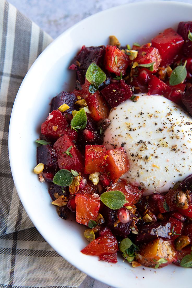 a white bowl filled with food on top of a checkered table cloth next to a fork