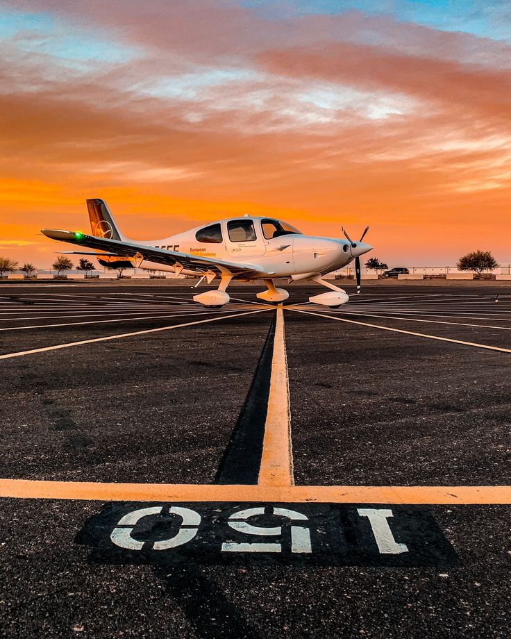 a small plane sitting on top of an airport tarmac with the sun setting in the background