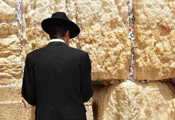 a man wearing a black suit and hat standing in front of the western wall