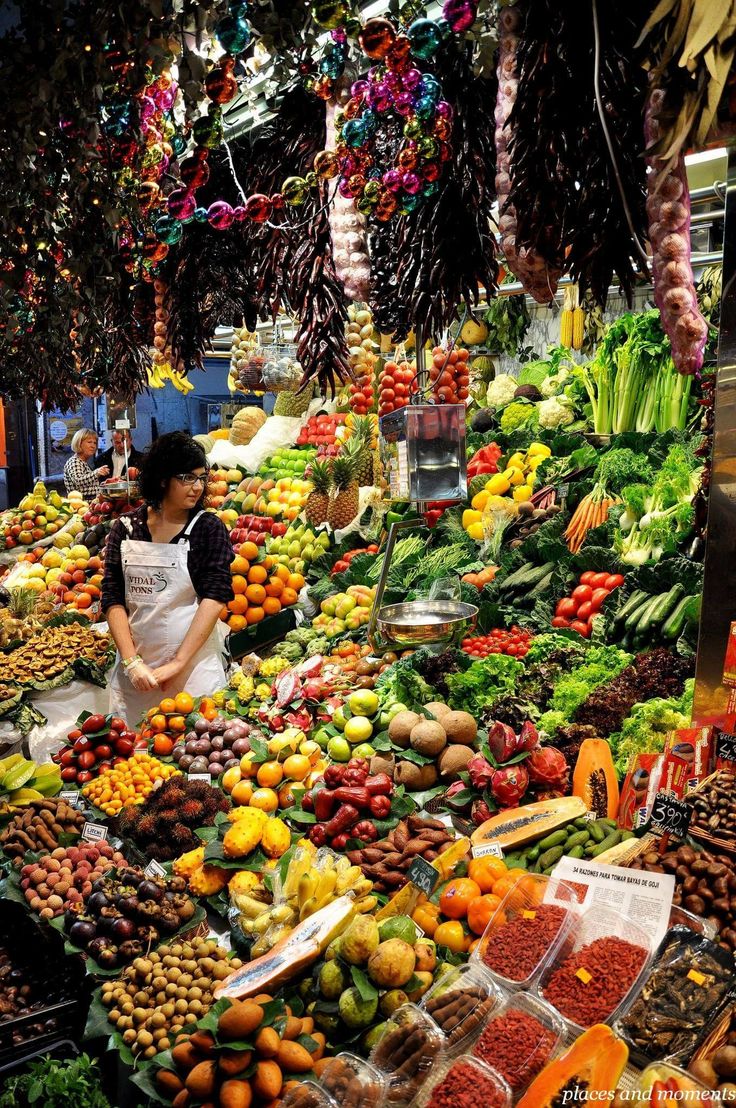 a woman standing in front of a large display of fruits and vegetables at a market