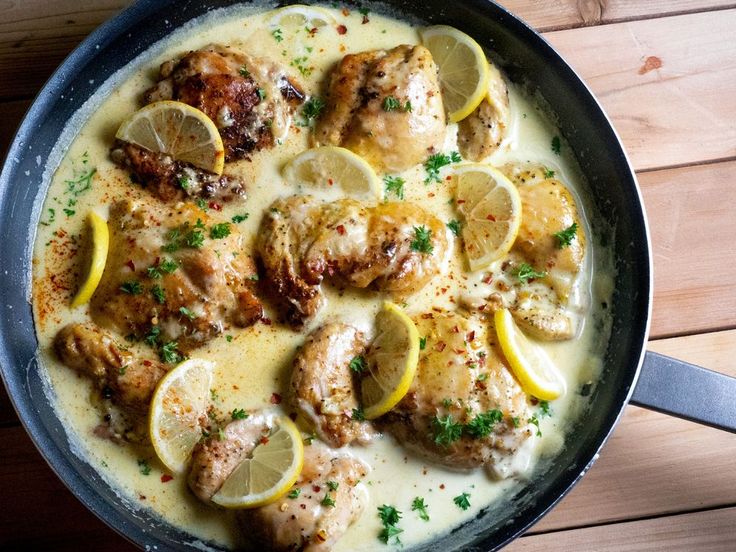 a pan filled with chicken and lemons on top of a wooden table