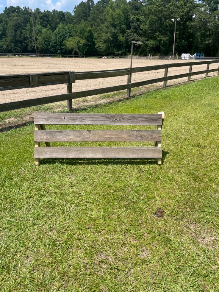 a wooden bench sitting on top of a lush green field next to a metal fence