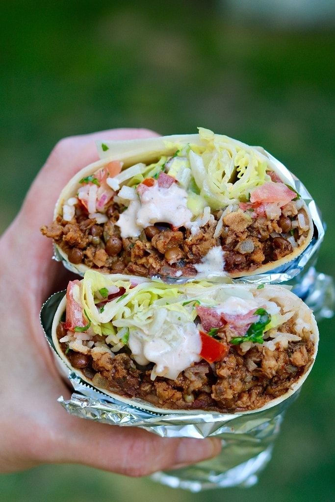 two burritos with meat, cheese and lettuce are held in their hands