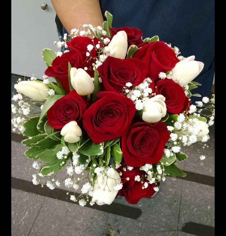 a bouquet of red roses and white tulips in someone's hand on the sidewalk