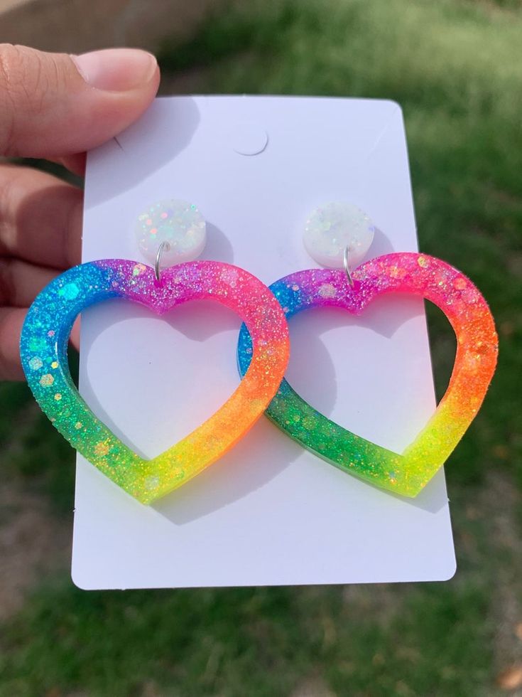 two rainbow colored heart shaped earrings on top of a white card