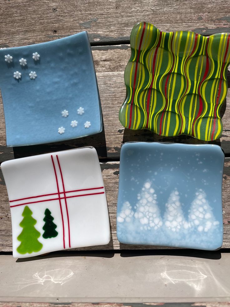 four decorative glass plates sitting on top of a wooden table with snowflakes and trees painted on them