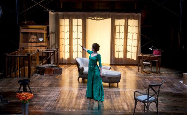 a woman in a green dress standing on a stage next to a couch and chair