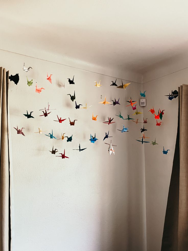 there are many origami birds hanging on the wall next to curtains in this room