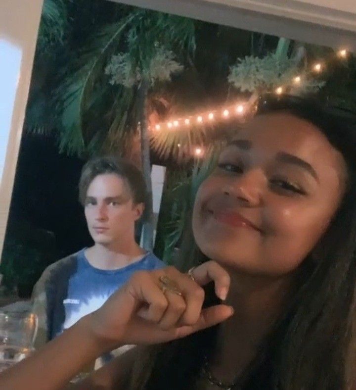 a girl is smiling and holding a piece of food in front of her face while another man looks on