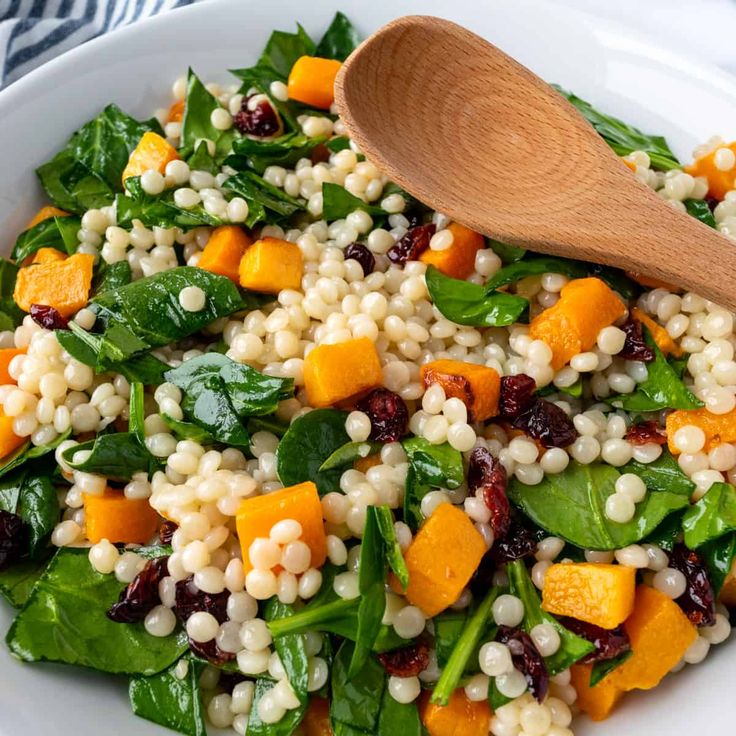 a salad with spinach, carrots, corn and cranberries in a white bowl