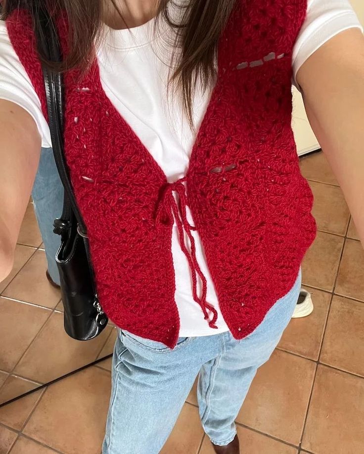 a woman wearing a red crocheted vest and jeans