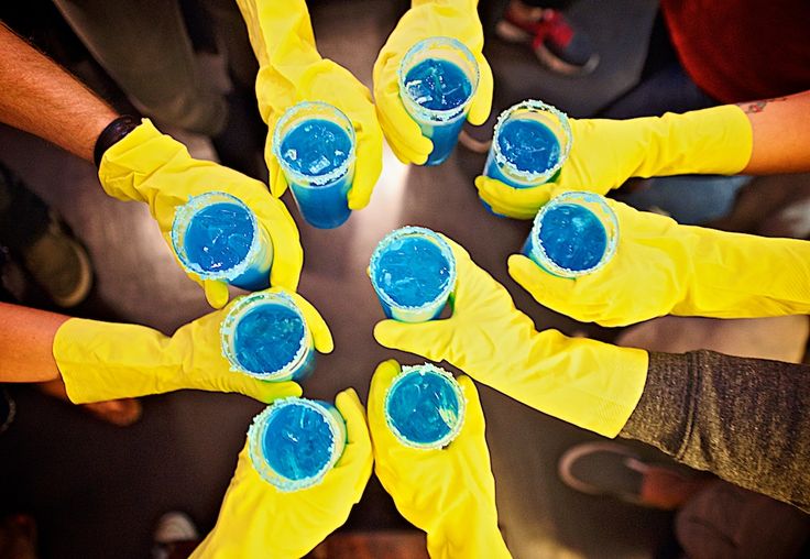 several people in yellow gloves are holding cups with blue liquid on them and looking up at the camera