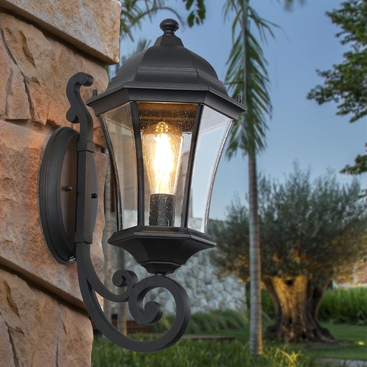 a light that is on the side of a wall next to a tree and grass