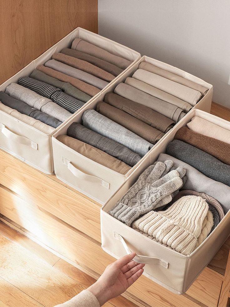 the drawers are filled with folded sweaters and socks, while someone's hand reaches for them