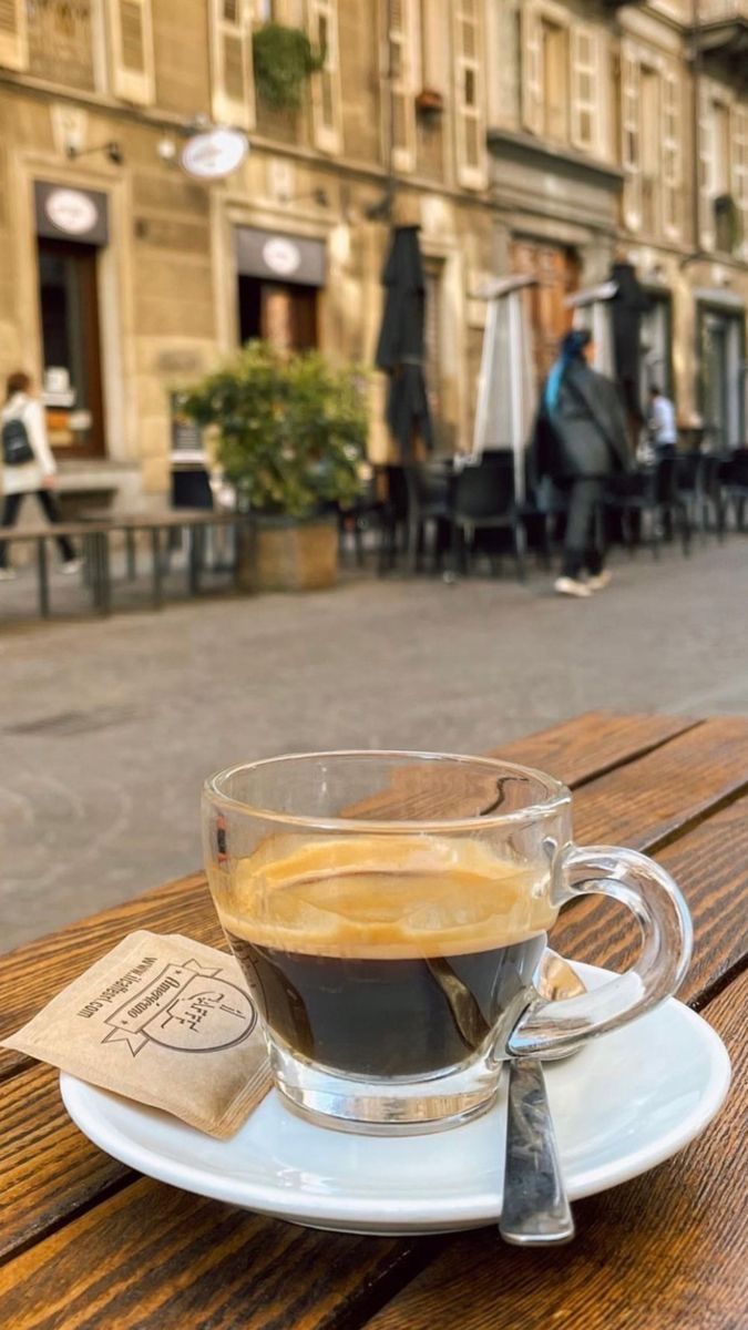 a cup of coffee sitting on top of a wooden table in front of a building