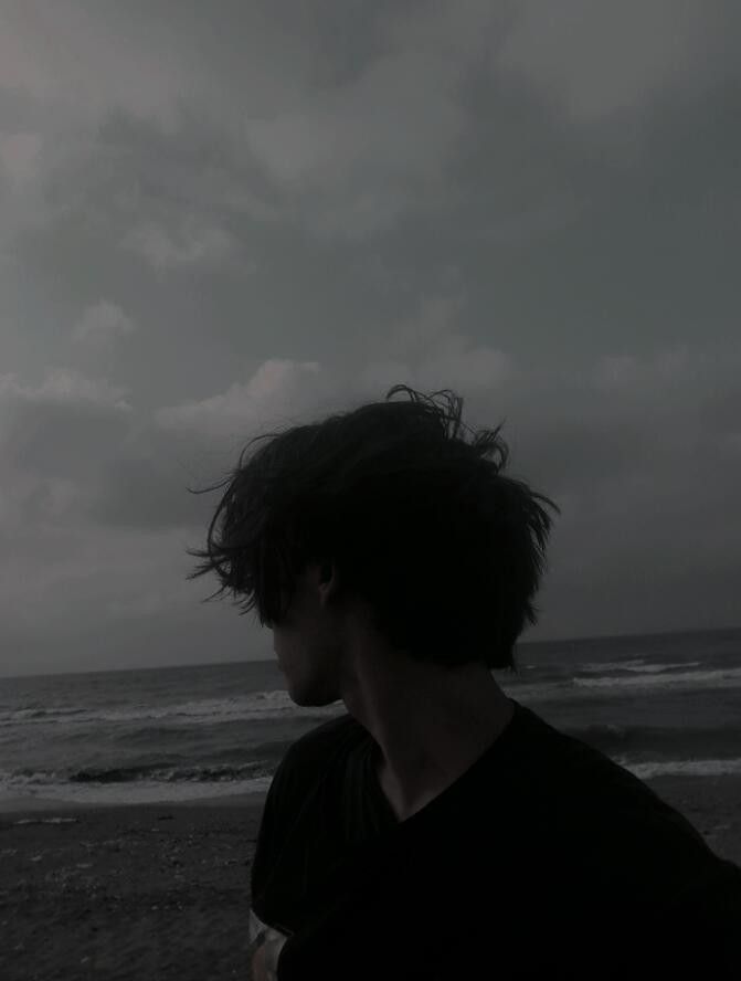 a man standing on top of a beach next to the ocean under a cloudy sky