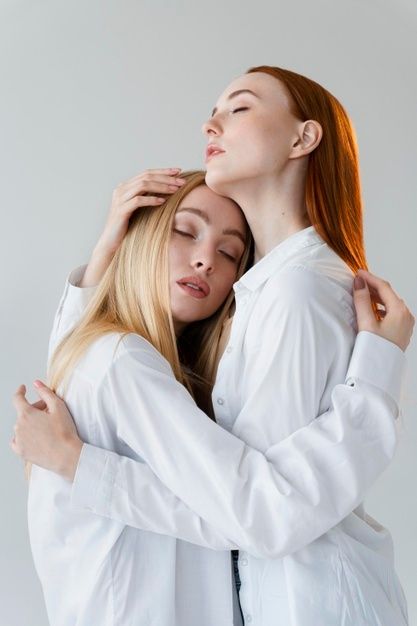 two beautiful young women hugging each other in front of a white background, both wearing white coats