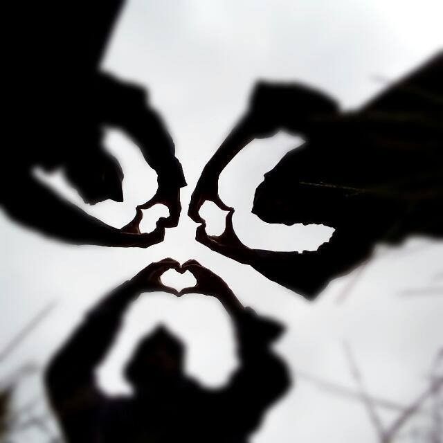 two hands making a heart shape with their fingers in the air and trees behind them