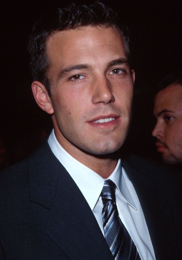 a close up of a person wearing a suit and tie with other people in the background