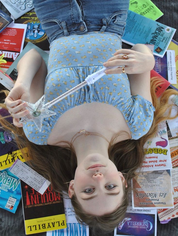 a woman laying on top of a pile of books and magazines next to a toothbrush