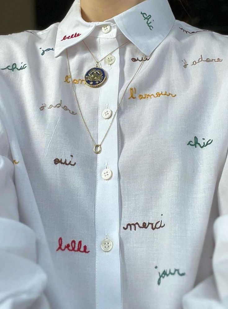 a woman wearing a white shirt with colorful writing on the front and back buttons down her chest