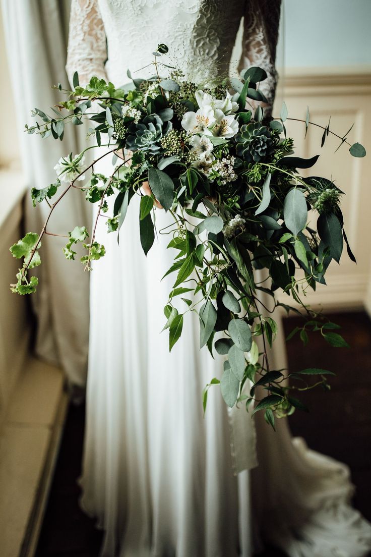 a bride holding a bouquet of greenery and white flowers in her wedding day dress