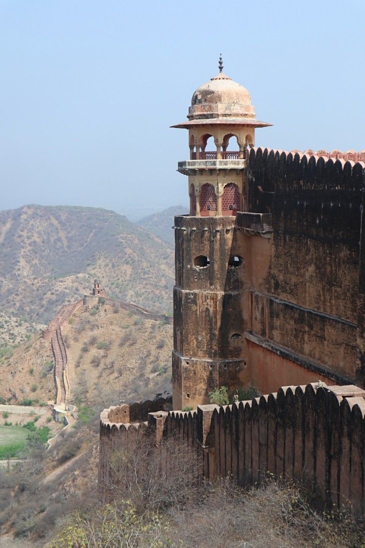 an old building on the side of a hill with mountains in the backgroud