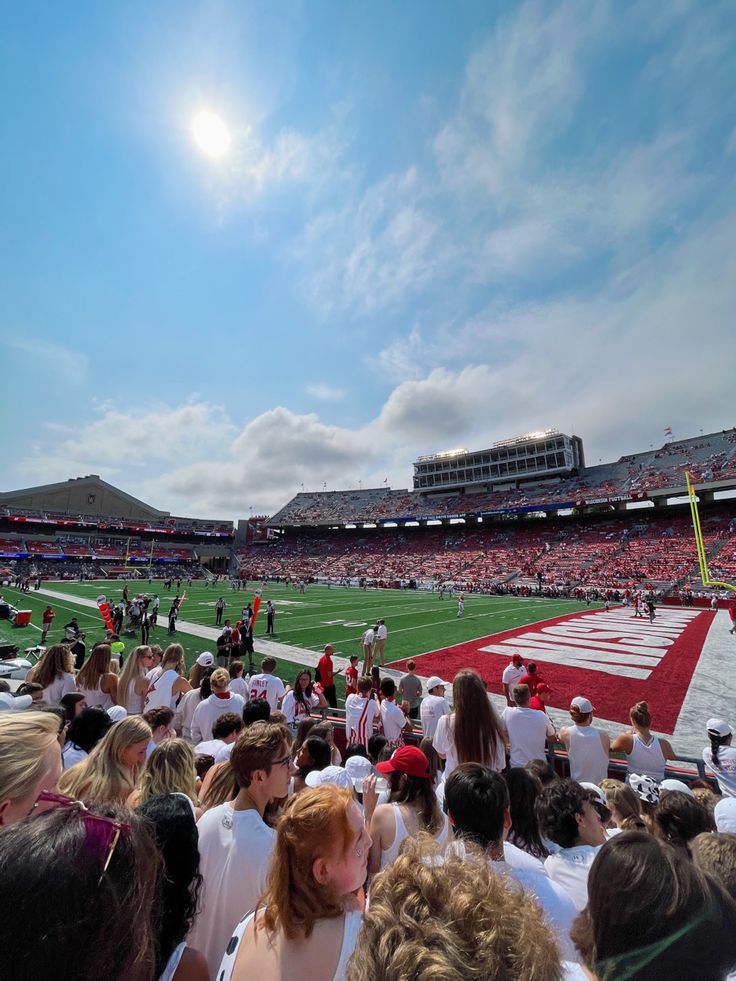 a group of people sitting on top of a field next to a football stadium filled with fans