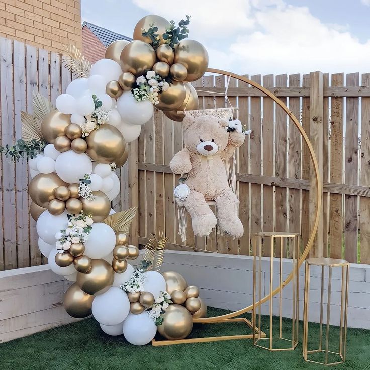 a teddy bear sitting on top of a balloon arch