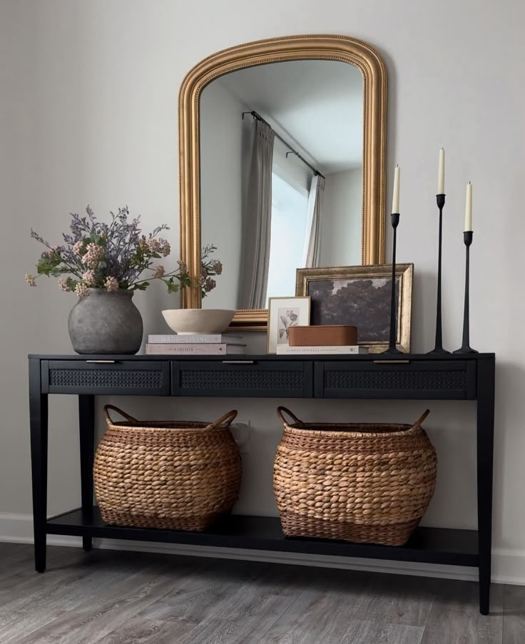 a console table with two baskets on it and a mirror in the corner next to it